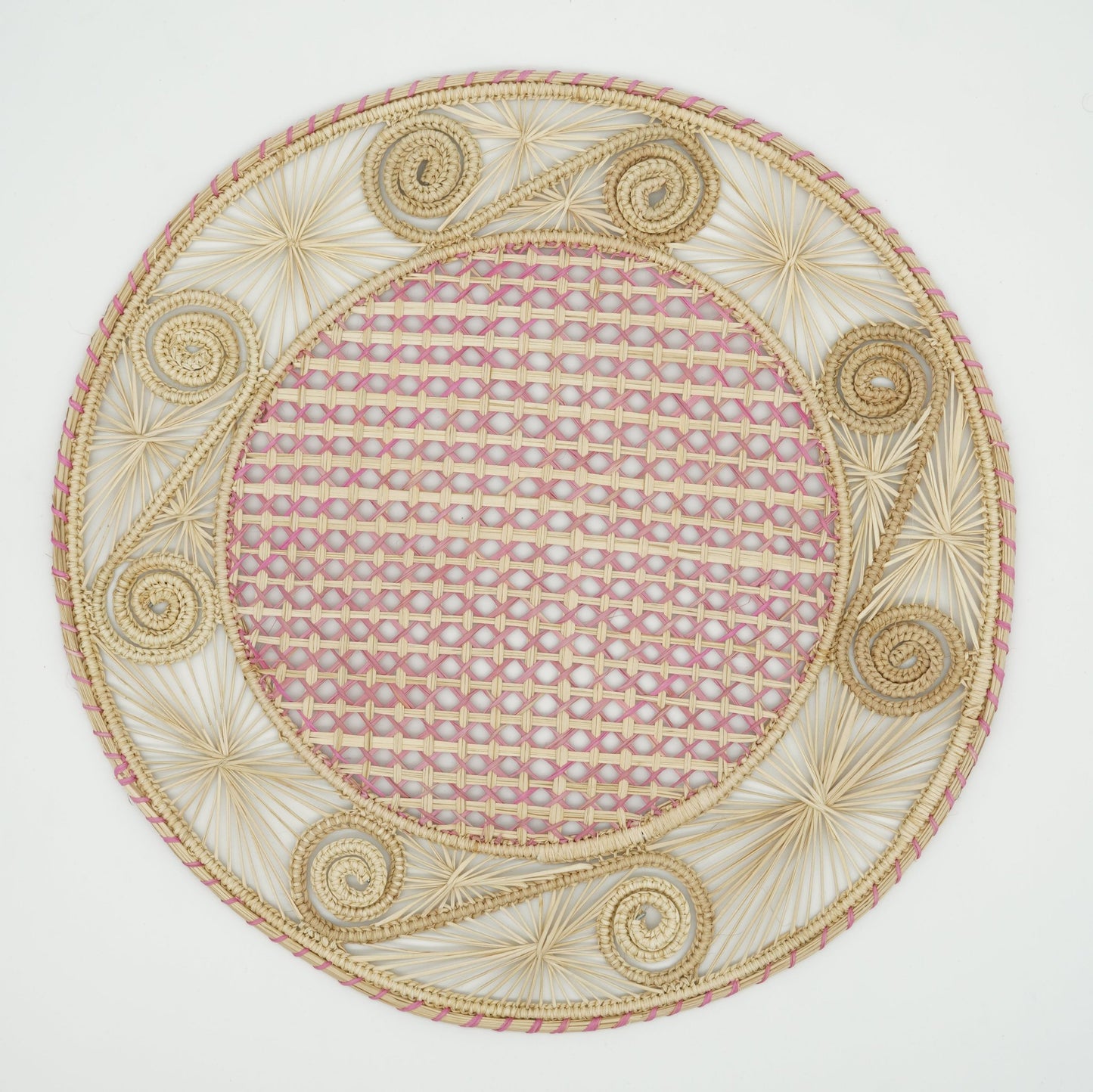 An overhead view of a woven placemat with a caracol (snail shell) pattern in natural and pink.