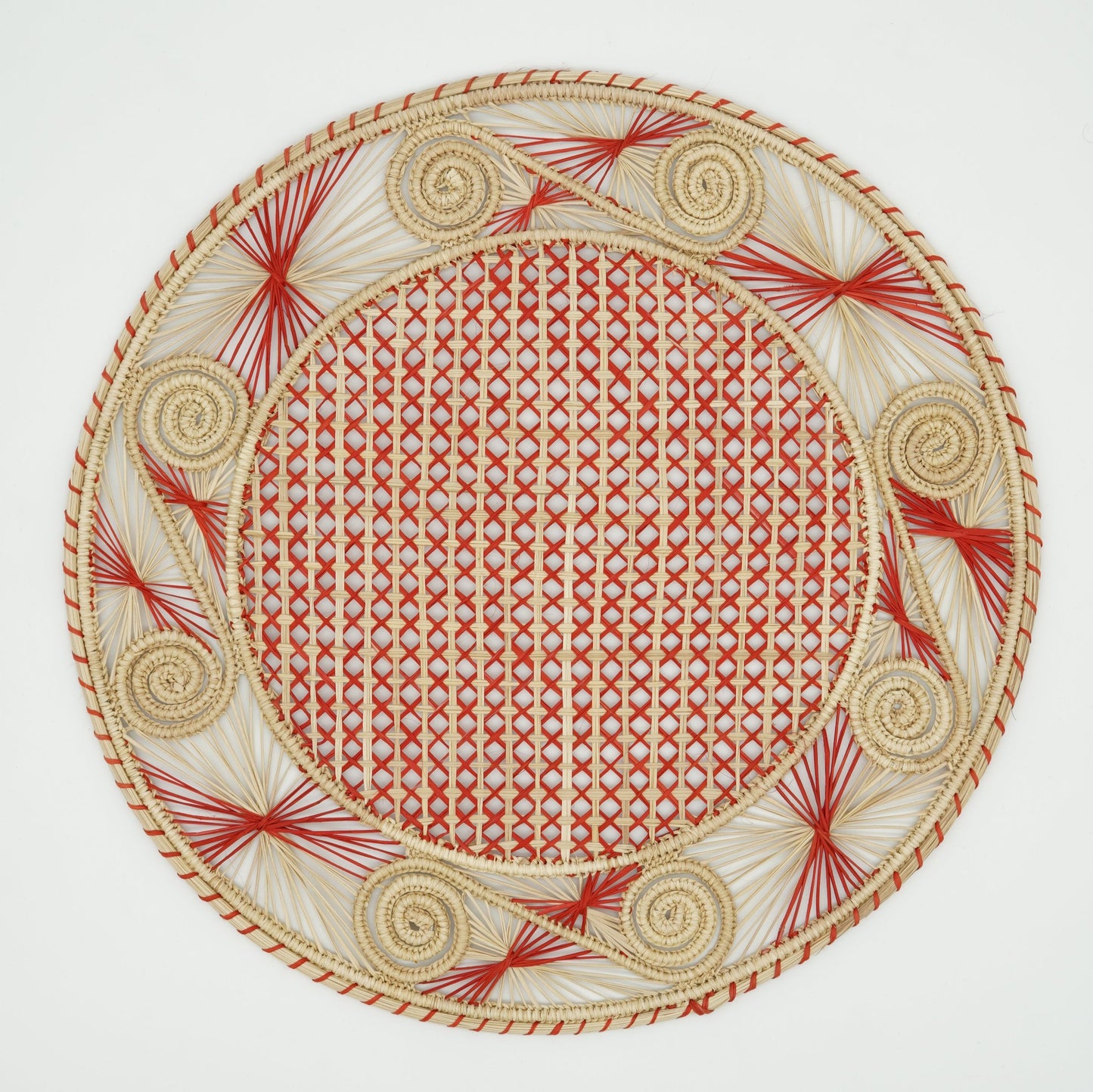 An overhead view of a woven placemat with a caracol (snail shell) pattern in natural and red.