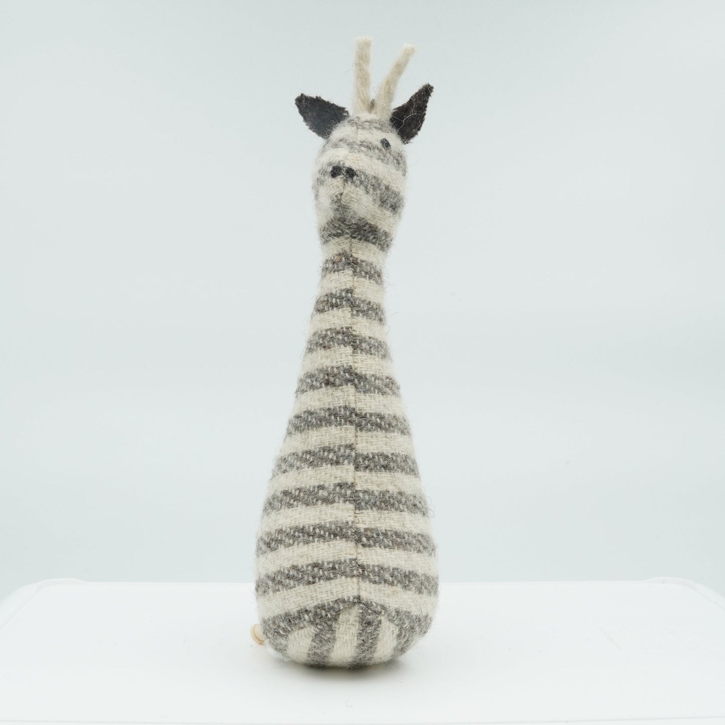 A gray and white wool rattle in the shape of a giraffe.