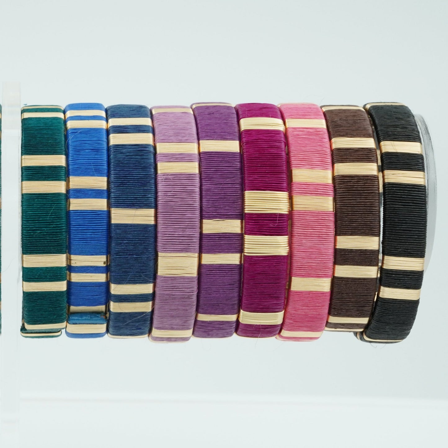 Bracelets made of werregue palm fiber and gold wire in deep aqua, blues, purples, pinks, brown, and black colors.