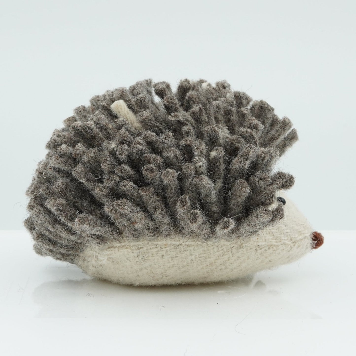 A side view of a gray and white wool rattle in the shape of a hedgehog.