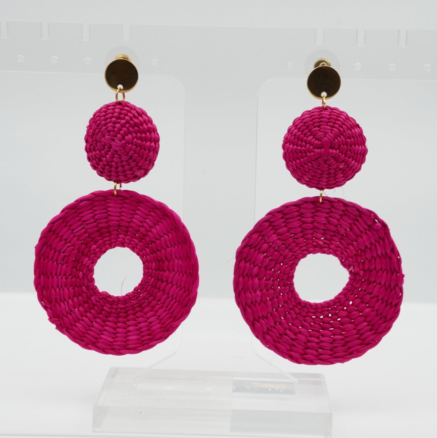 Head on view of iraca fuchsia circle and dot woven earrings.