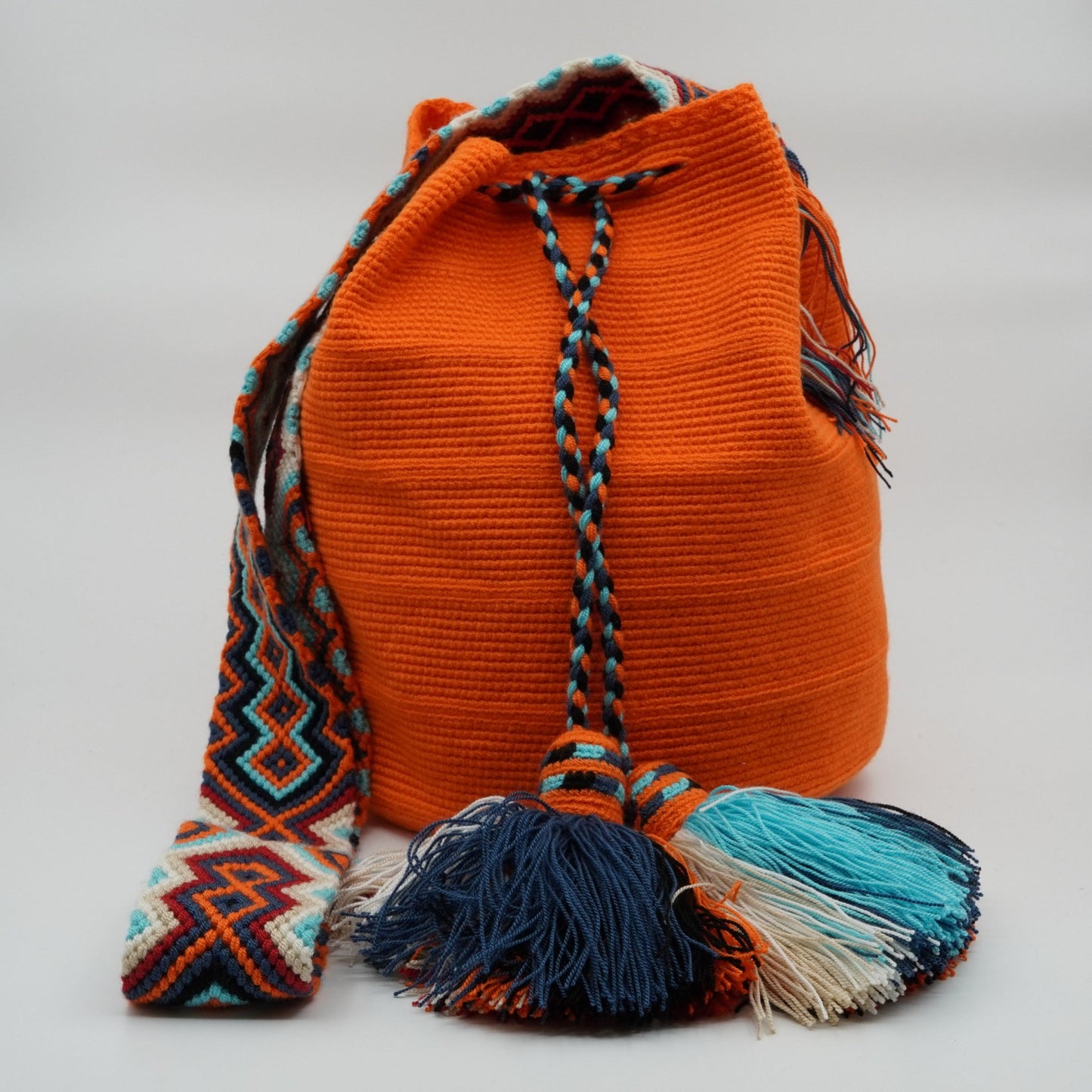 Large orange mochila woven handbag with pompoms.
