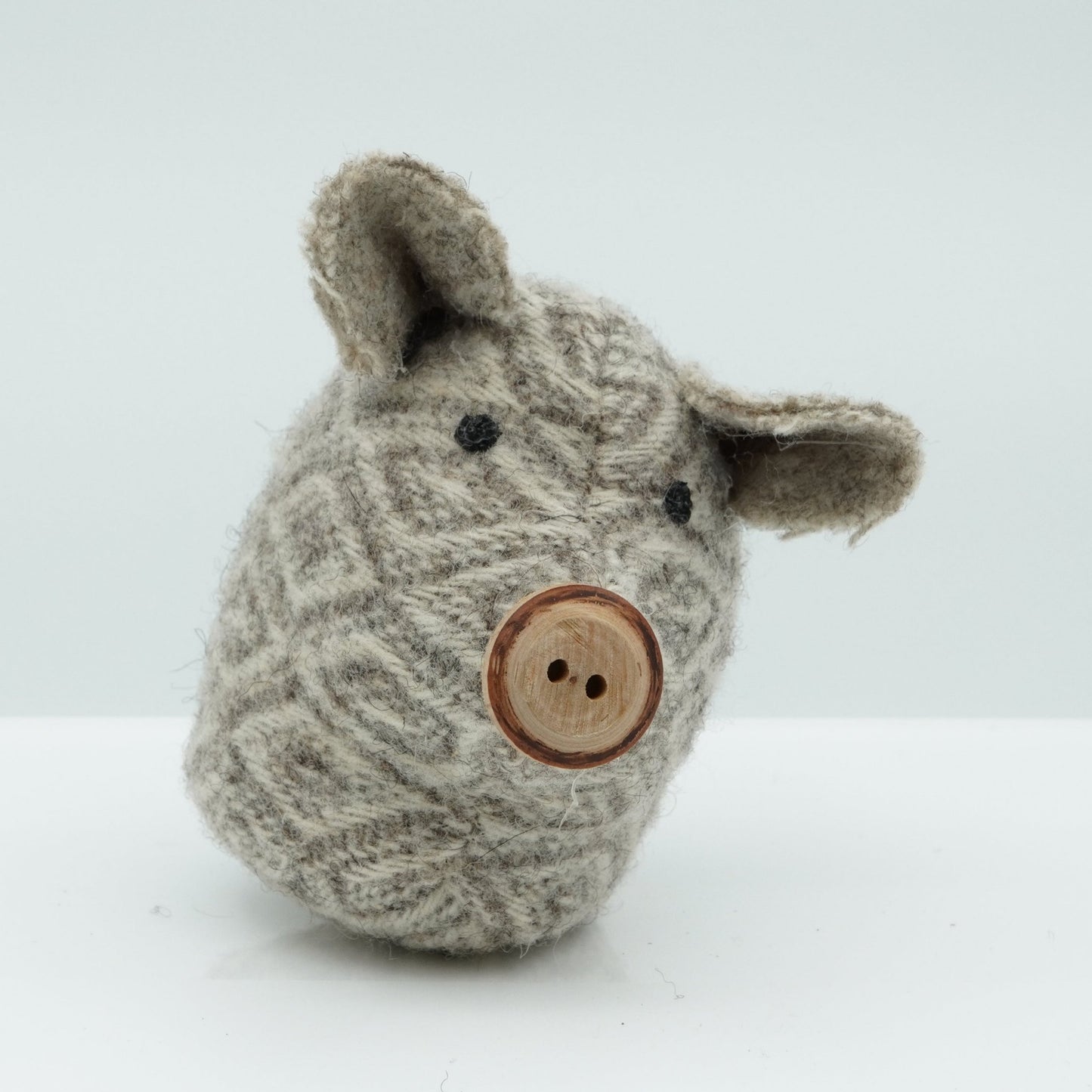 A side view of a gray and white wool rattle in the shape of a pig.