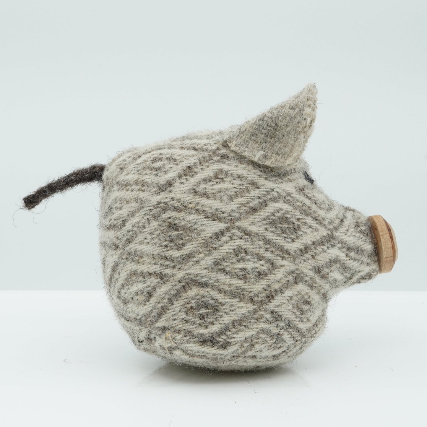 A side view of a gray and white wool rattle in the shape of a pig.