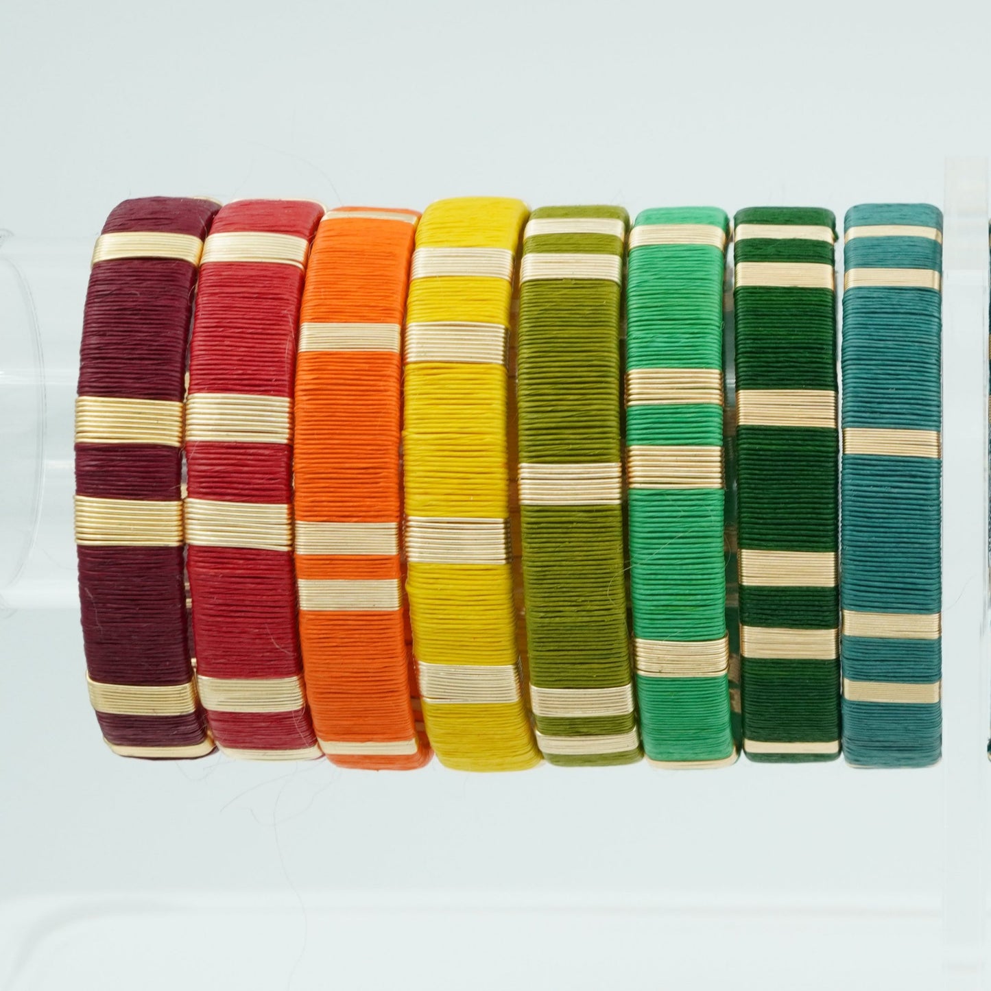 Bracelets made of werregue palm fiber and gold wire in wine, red, orange, yellow, and green colors.