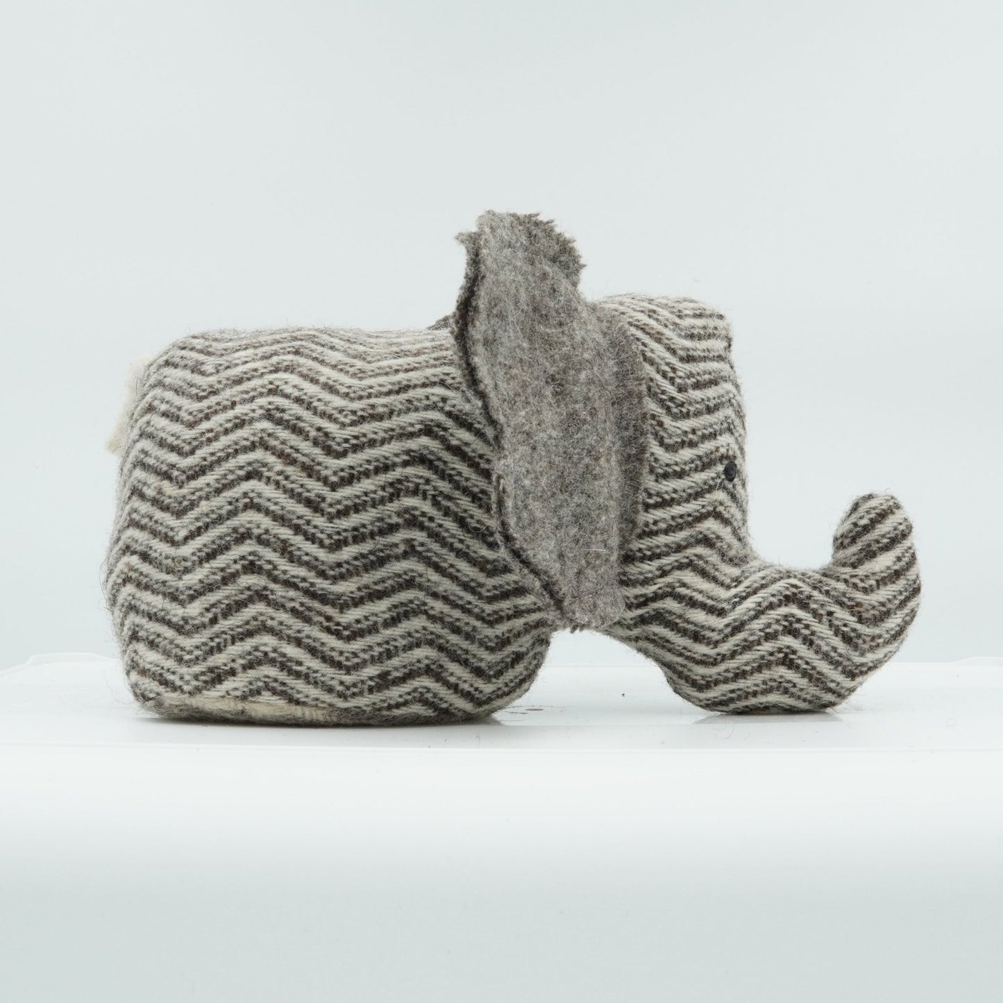 A side view of a gray and white wool doorstop in the shape of a small elephant.