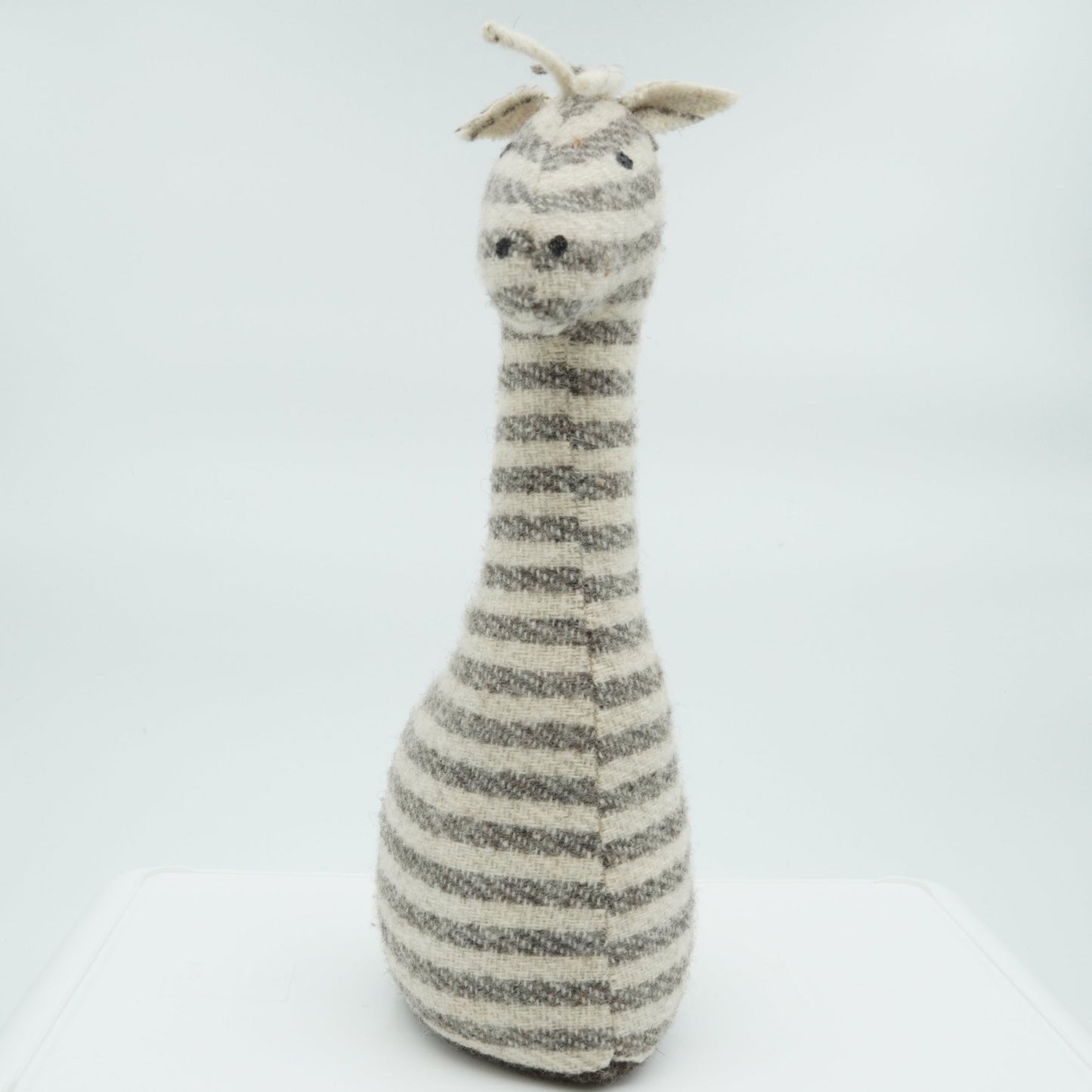 A gray and white wool doorstop in the shape of a small giraffe.
