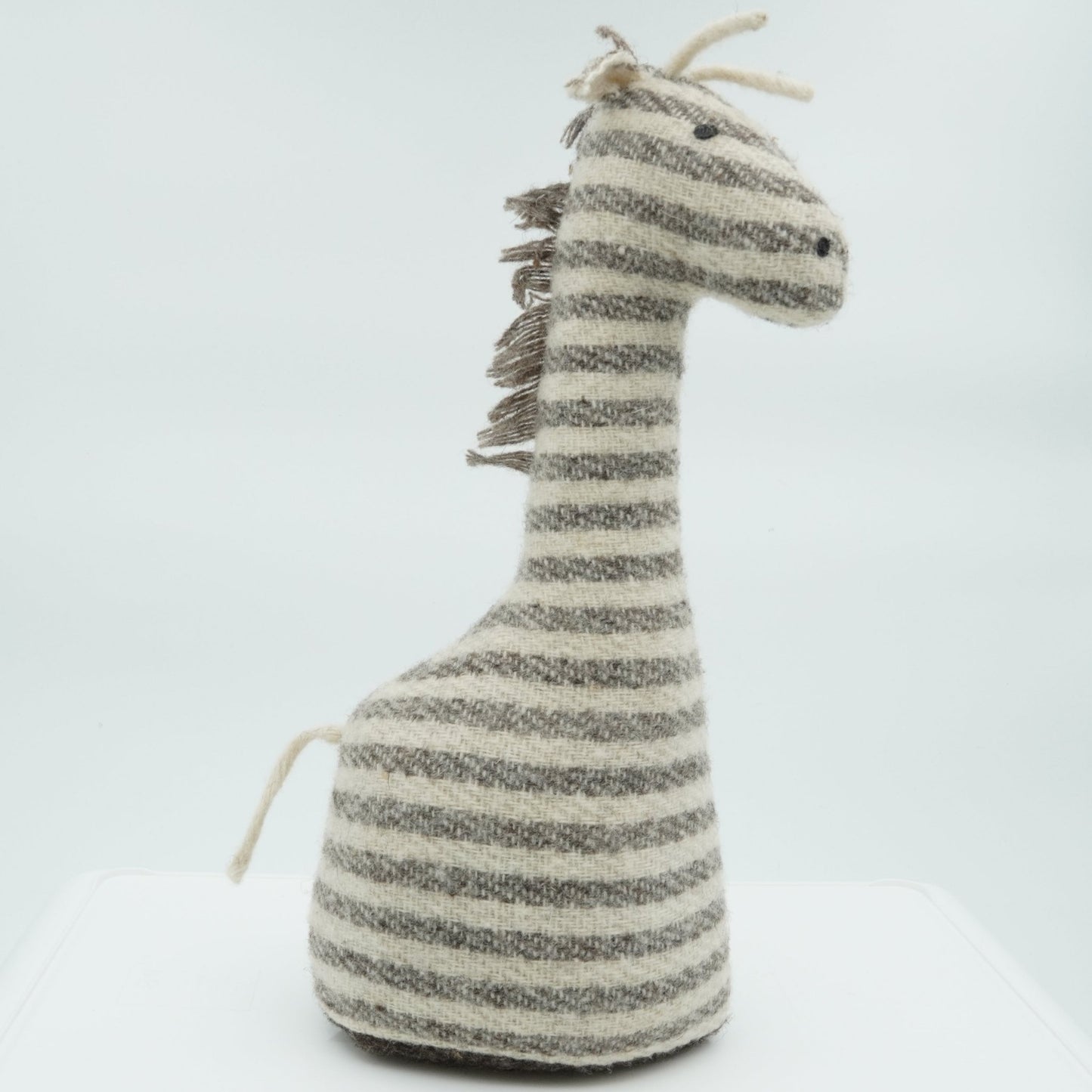 A side view of a gray and white wool doorstop in the shape of a small giraffe.