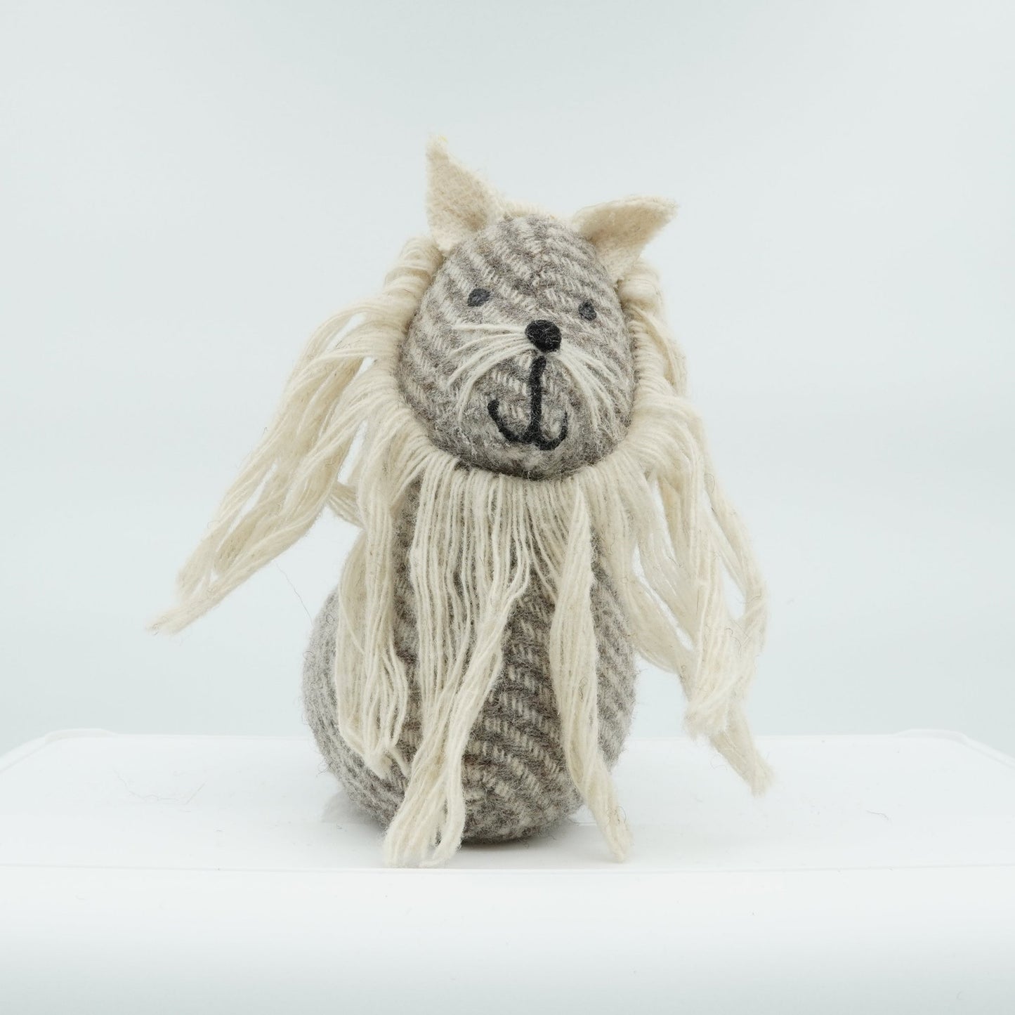 A gray and white wool doorstop in the shape of a small lion.