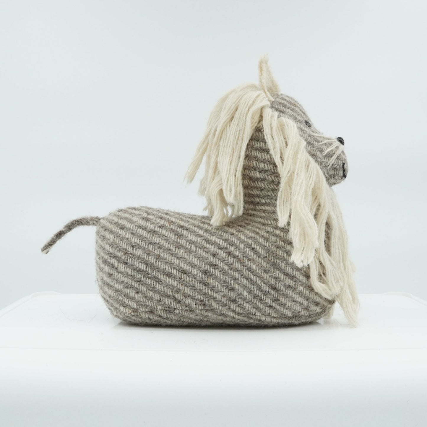 A side view of a gray and white wool doorstop in the shape of a small lion.