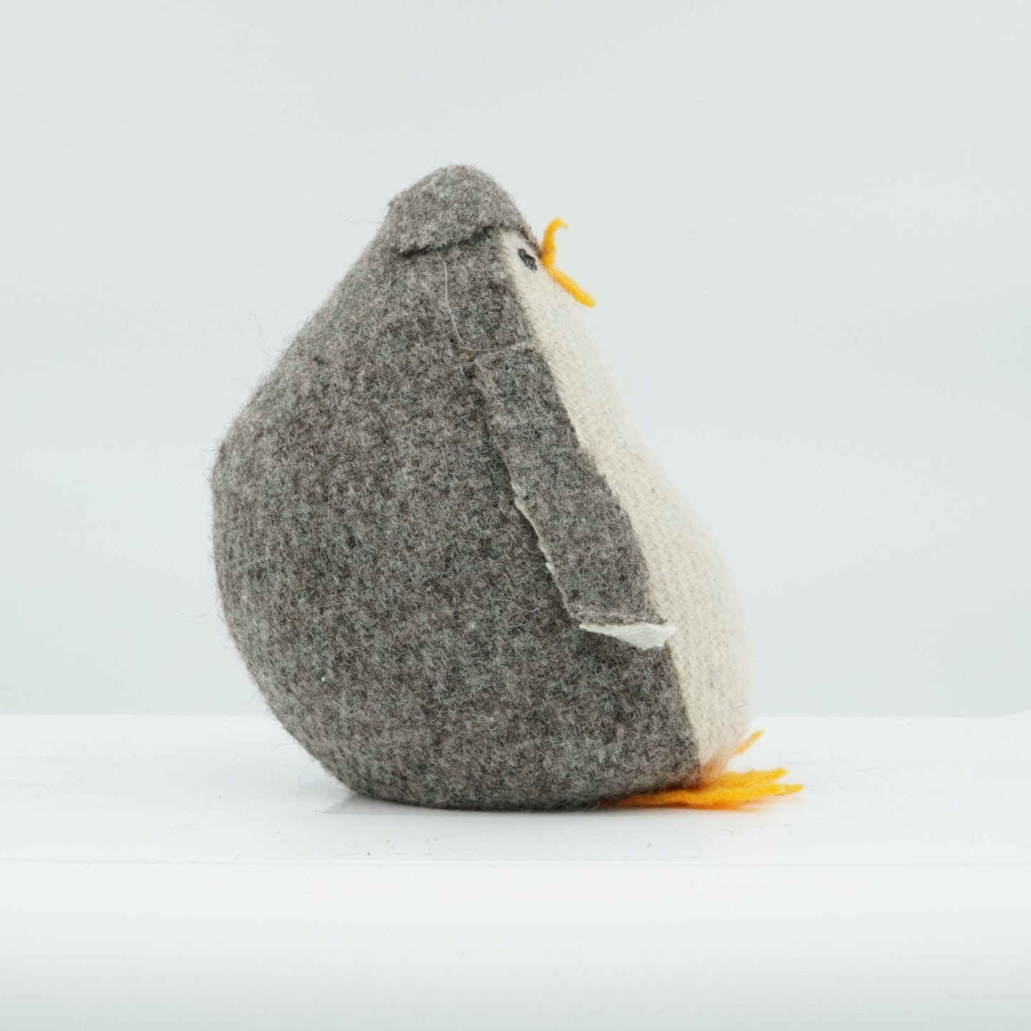 A side view of a gray and white wool doorstop in the shape of a small penguin.