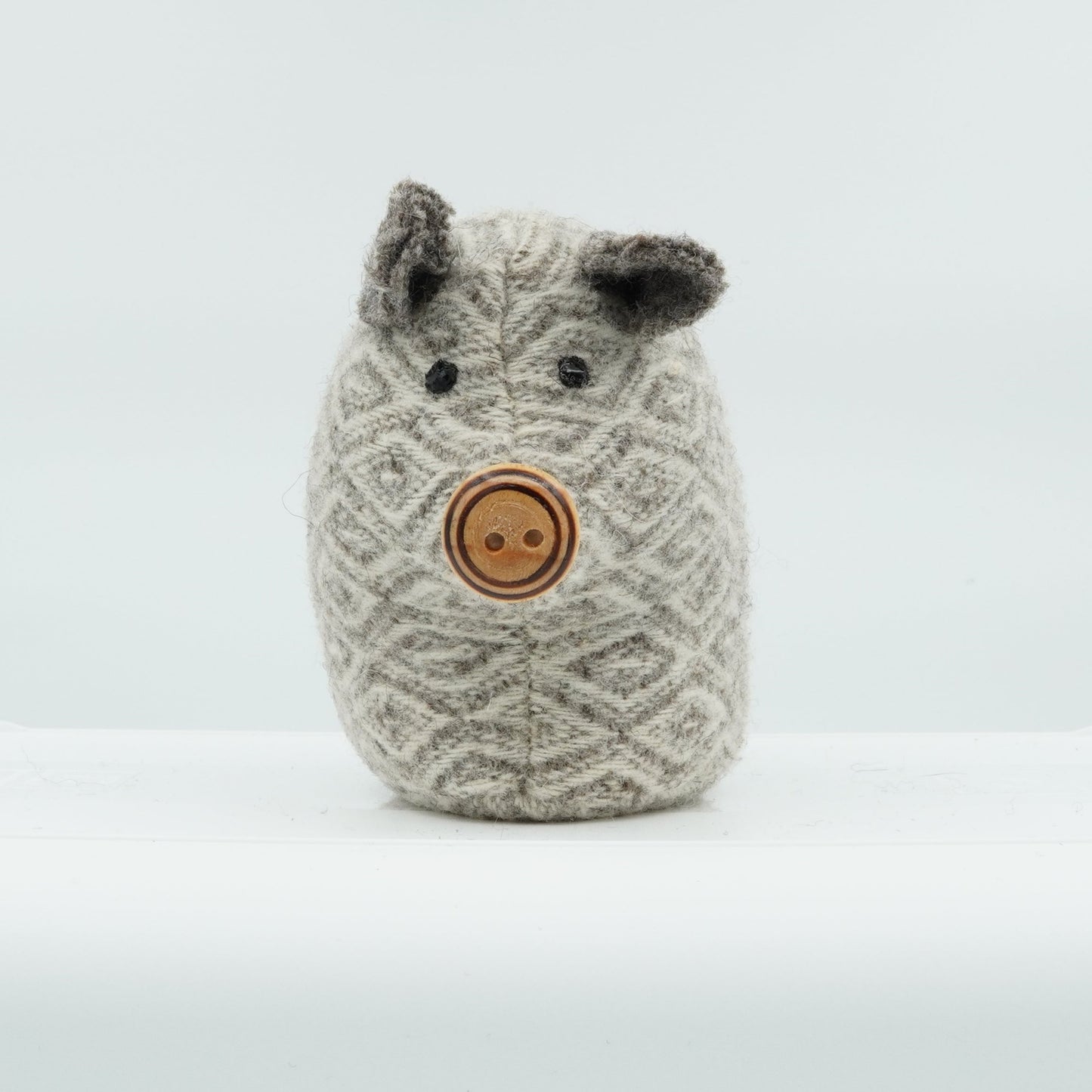 A gray and white wool doorstop in the shape of a small pig.