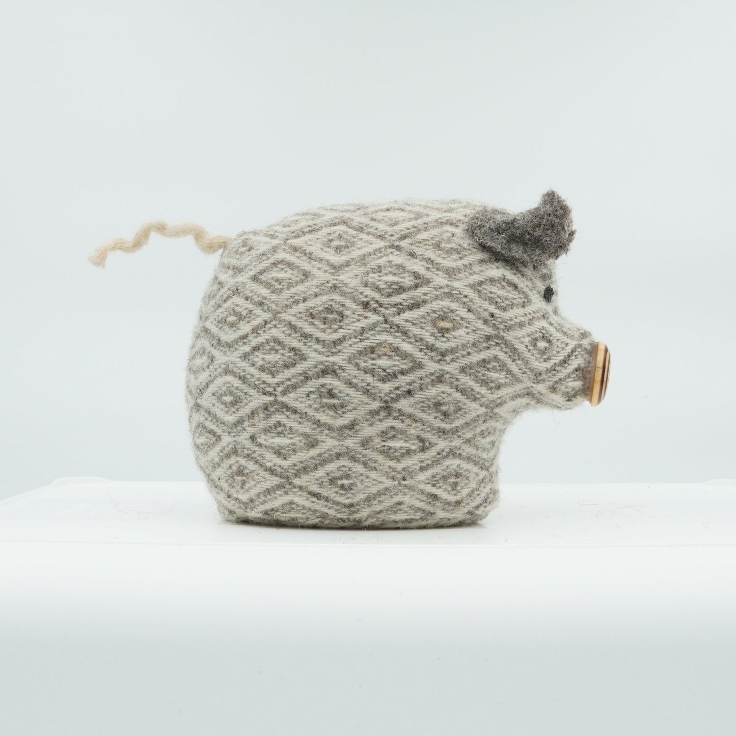 A side view of a gray and white wool doorstop in the shape of a small pig.