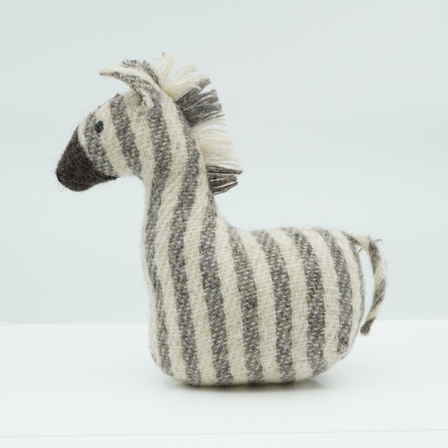 A side view of a gray and white wool rattle in the shape of a zebra.