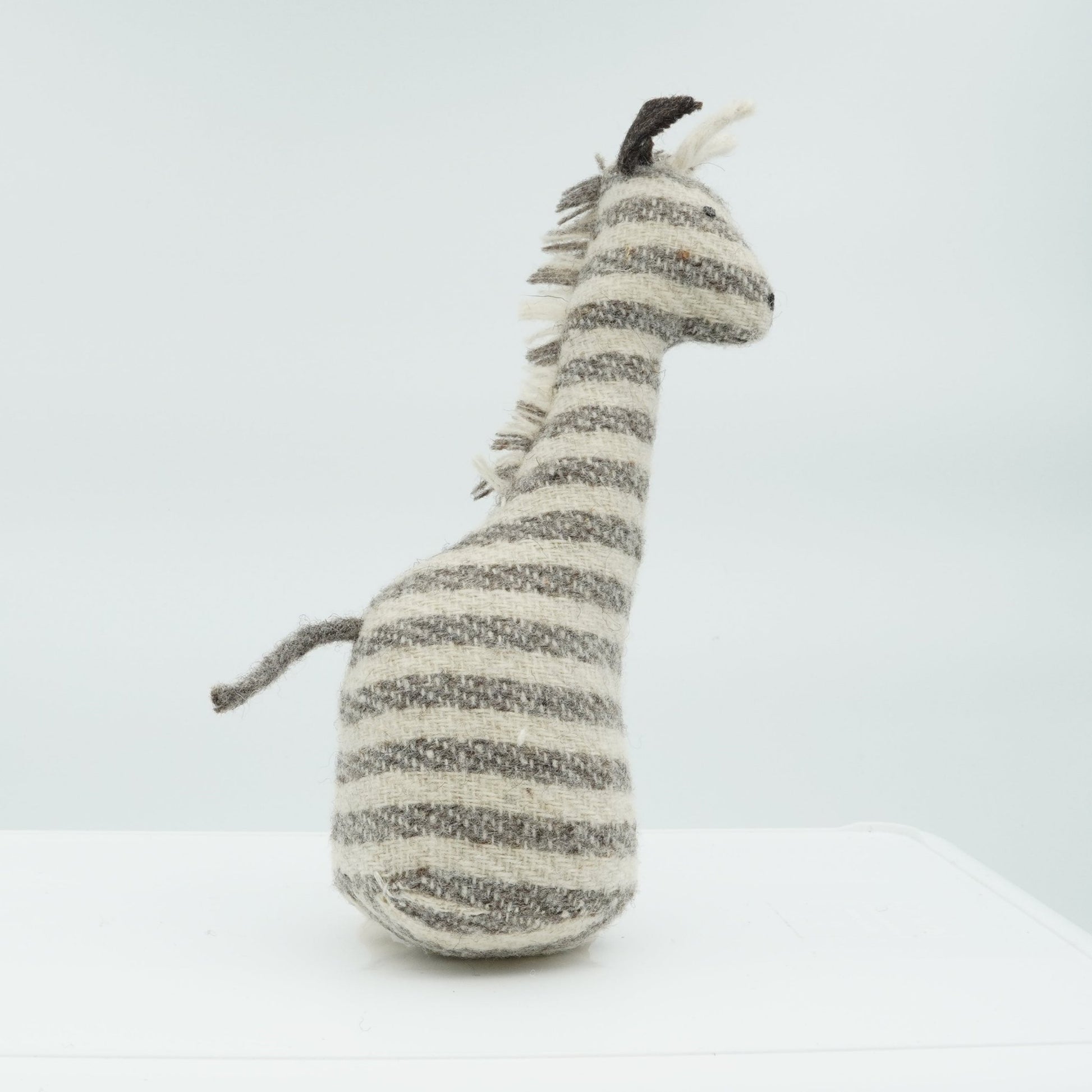 A side view of a gray and white wool rattle in the shape of a giraffe.