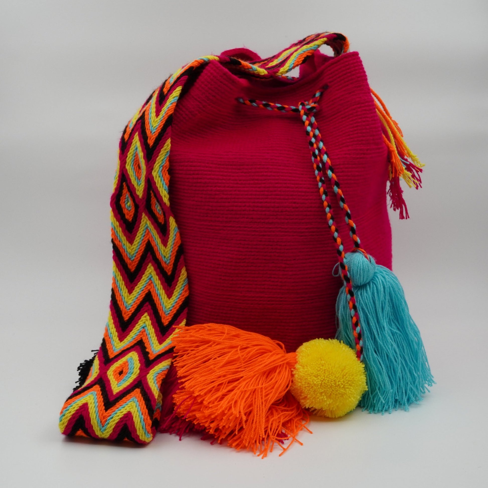 Large fuchsia mochila woven handbag with pompoms.