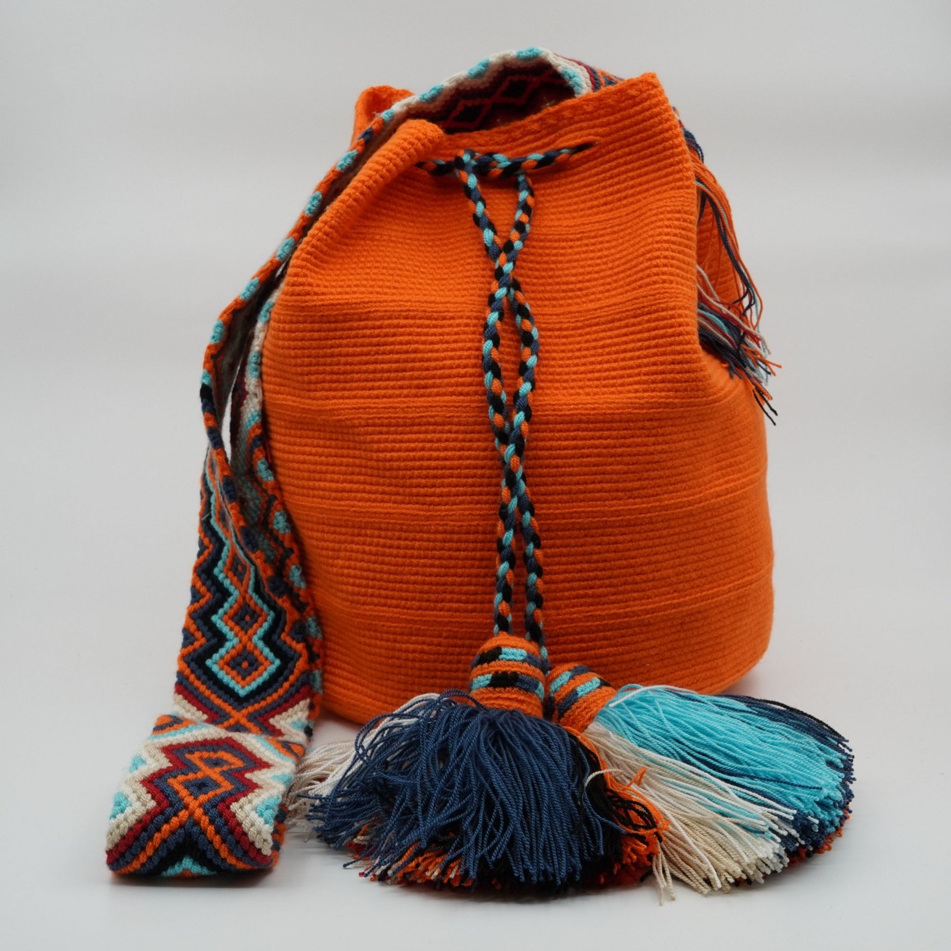 Large orange mochila woven handbag with pompoms.
